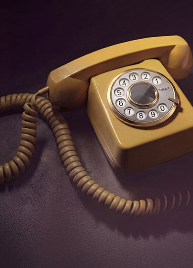 Vintage rotary telephone with a Timex-branded rotary dial displayed on a dark surface, featuring a coiled cord and warm retro lighting.