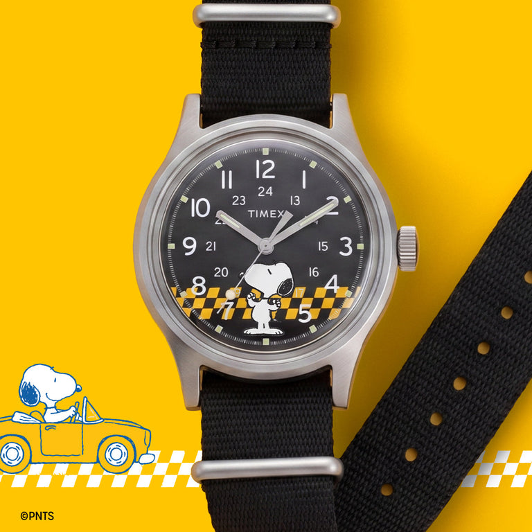 Peanuts® x Timex MK1® watch with a black dial, black fabric strap, and Snoopy racing graphic, displayed against a yellow racing-inspired background.