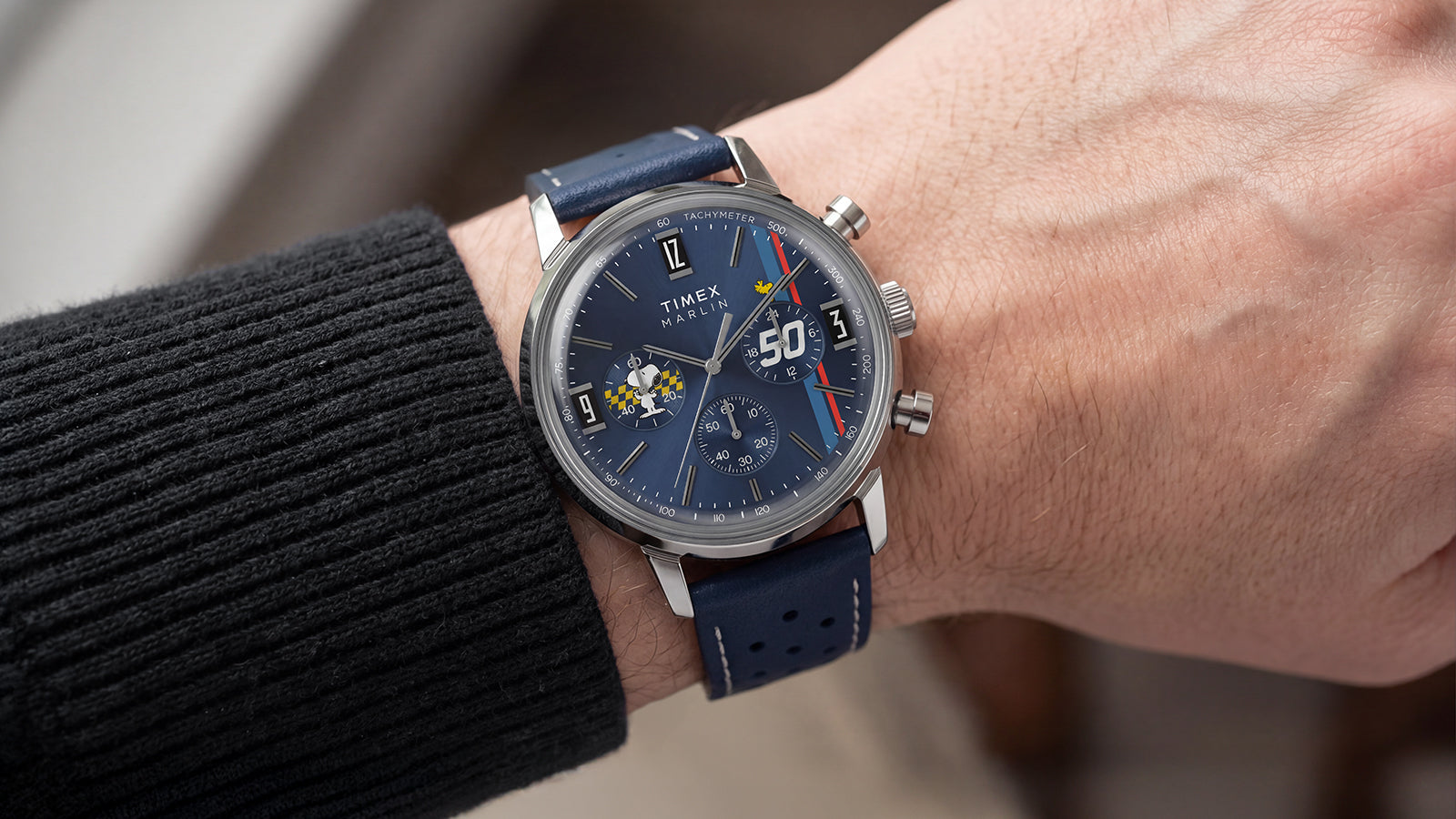 Peanuts® x Timex Marlin® Chronograph worn on the wrist, showcasing a blue dial, perforated blue leather strap, and Snoopy-themed chronograph design.