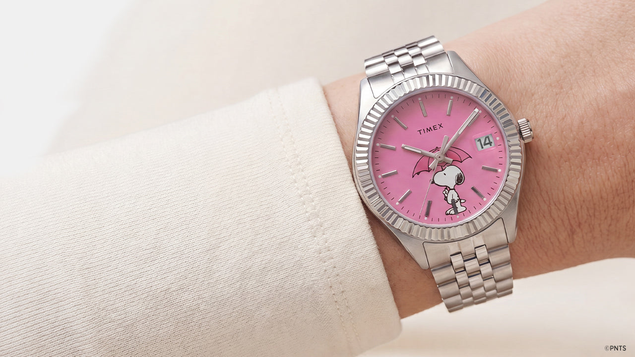Peanuts® x Timex Legacy Snoopy Umbrella watch worn on the wrist with a pink dial, stainless steel bracelet, and Snoopy umbrella artwork.