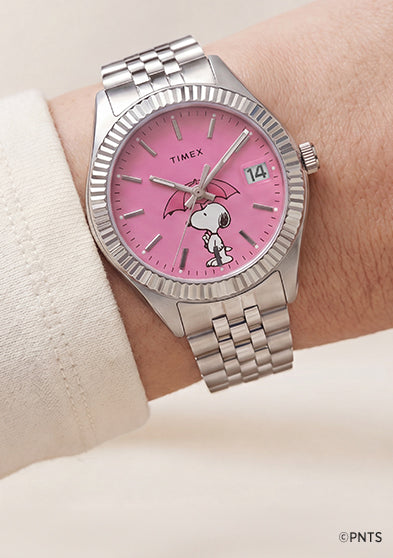 Peanuts® x Timex Legacy Snoopy Umbrella watch worn on the wrist with a pink dial, stainless steel bracelet, and Snoopy umbrella artwork.