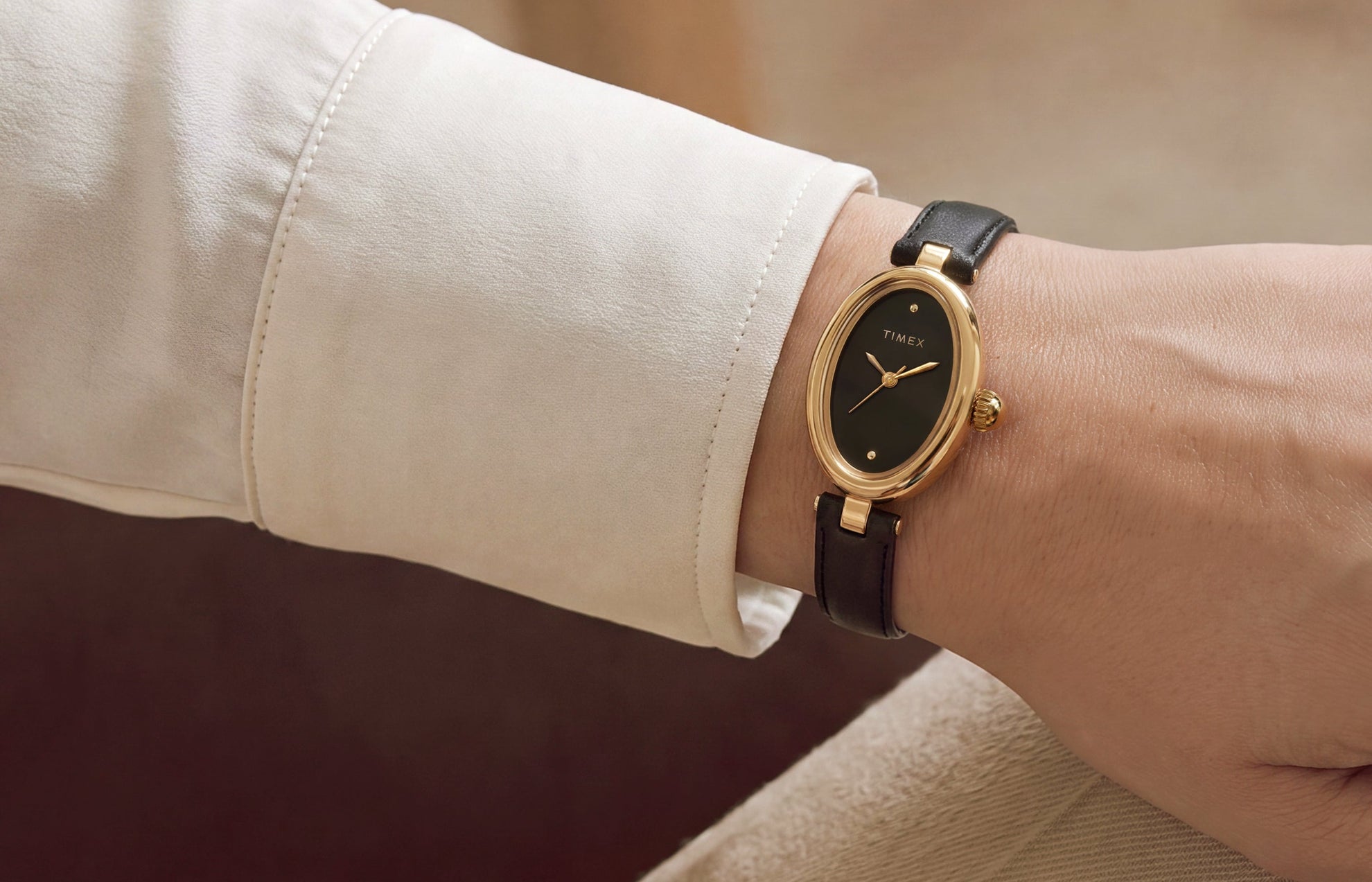 Close-up of the Timex Cavatina® Luxe with a gold-tone oval case, black dial, and black leather strap worn on the wrist.