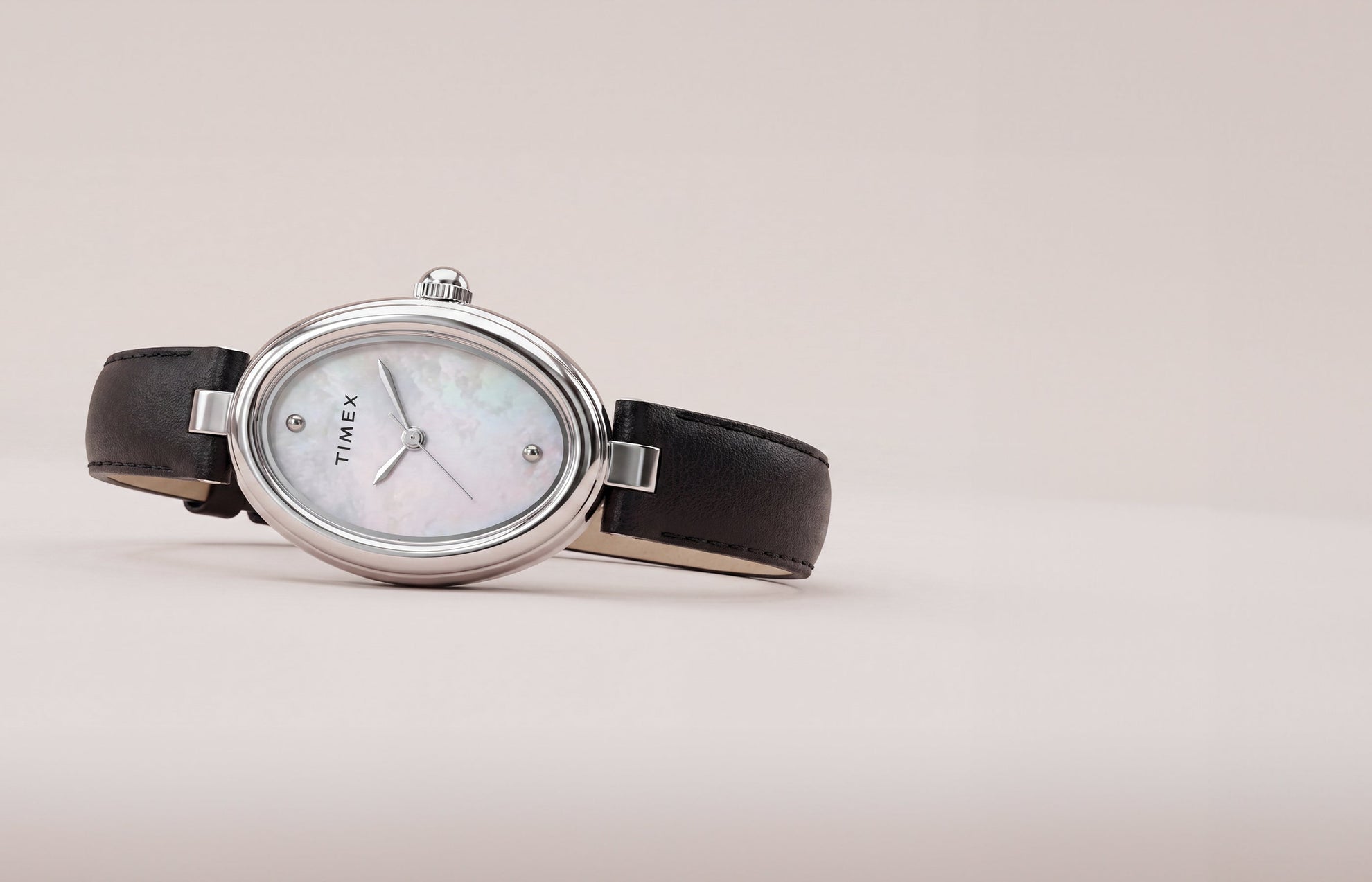 Timex Cavatina® Luxe watch with a silver-tone oval case, mother-of-pearl dial, and black leather strap displayed on a soft neutral background.