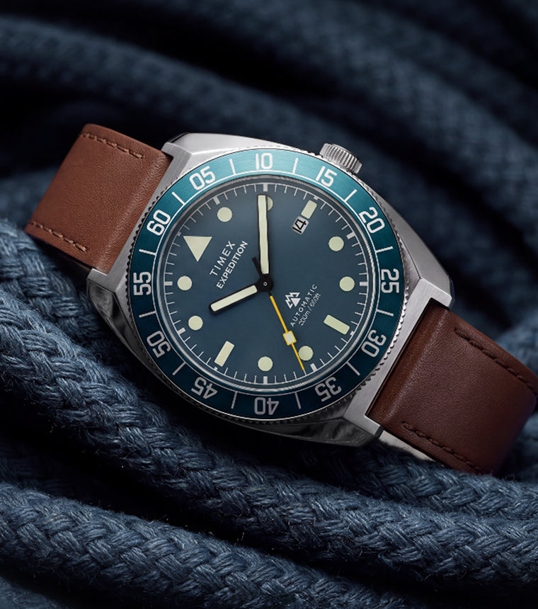 Timex Expedition Pioneer Automatic with a blue dial, blue rotating bezel, and brown leather strap displayed on coiled navy rope.