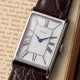 Close-up of the Timex 1976 Lexington Reissue Inspired watch featuring a silver sunray dial, black Roman numeral markers, blue hands, and a brown crocodile-grain leather strap.