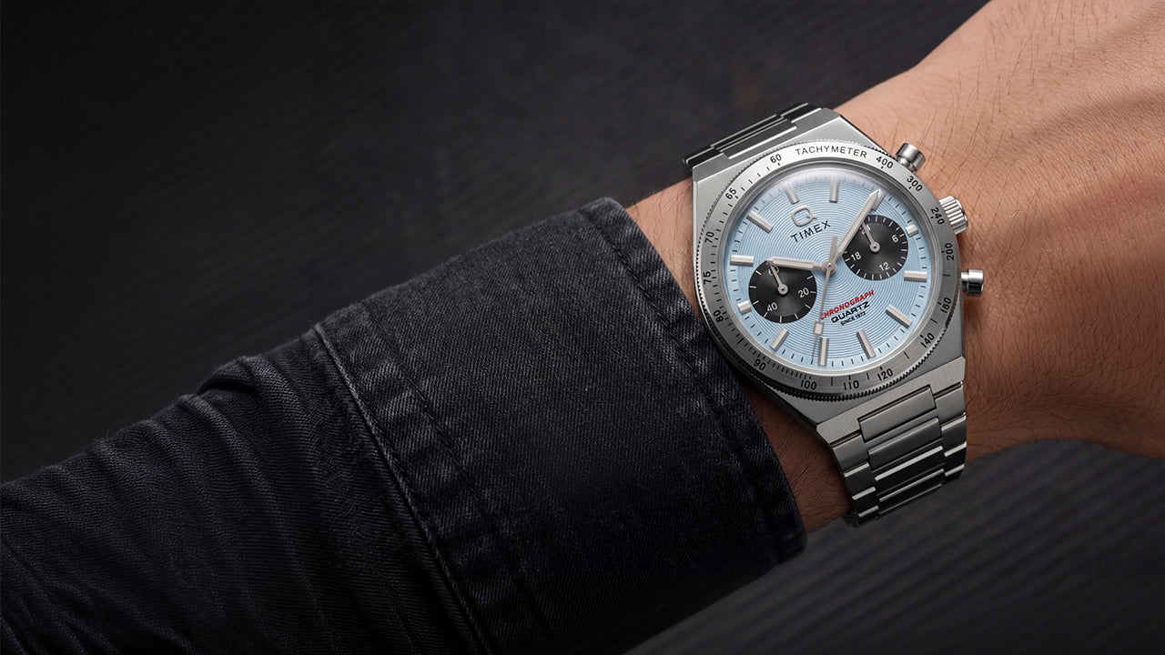 Q Timex Continental Chronograph worn on the wrist with a dark jacket, featuring an ice blue chronograph dial and stainless-steel bracelet.