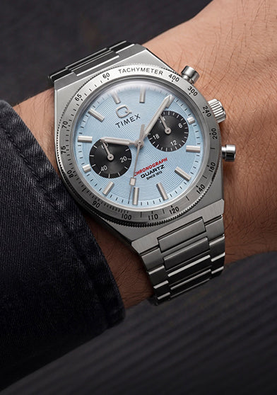 Q Timex Continental Chronograph worn on the wrist with a dark jacket, featuring an ice blue chronograph dial and stainless-steel bracelet.