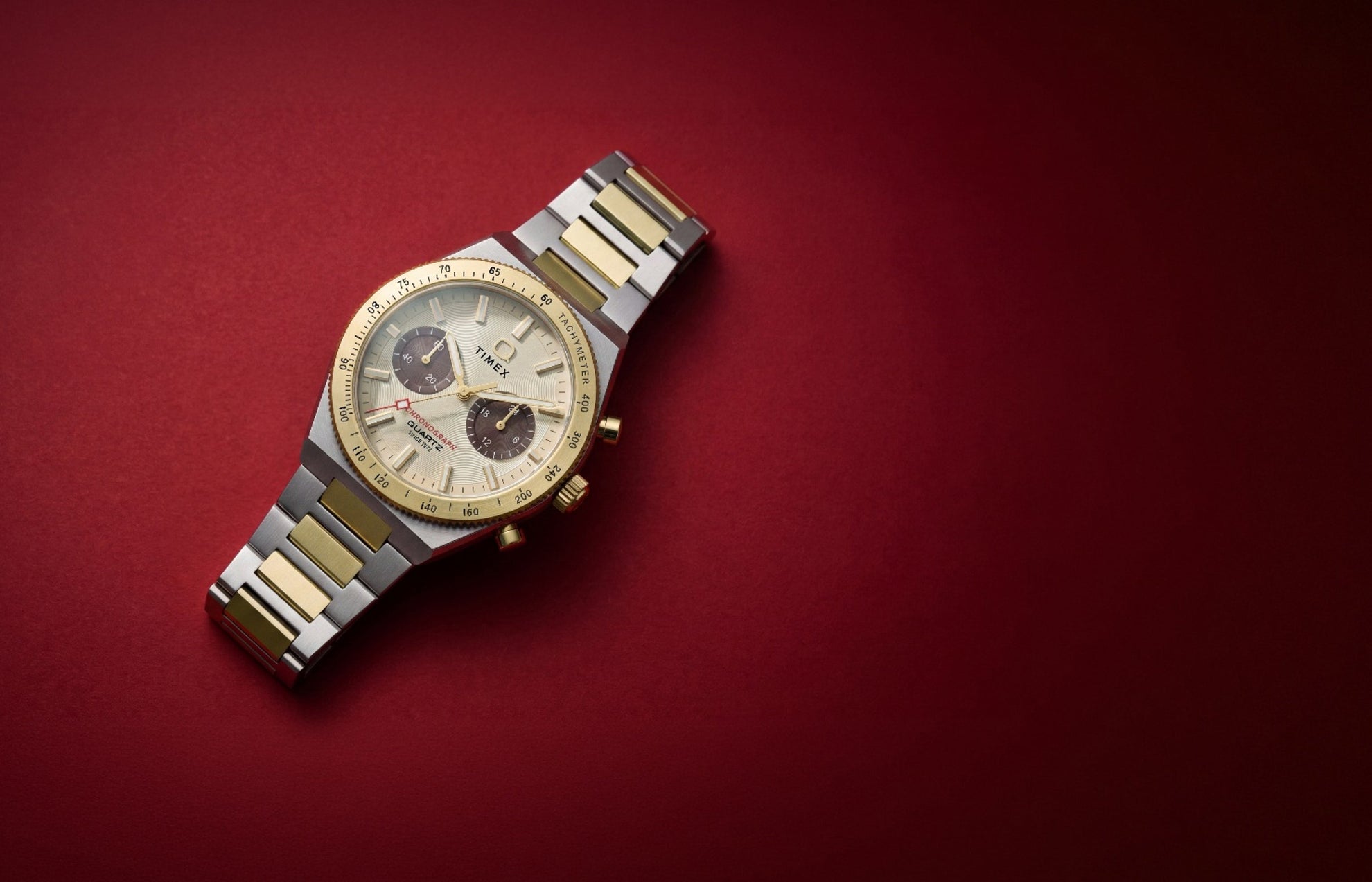 Q Timex Continental Chronograph two-tone watch with a gold-tone bezel and champagne dial on a deep red background.