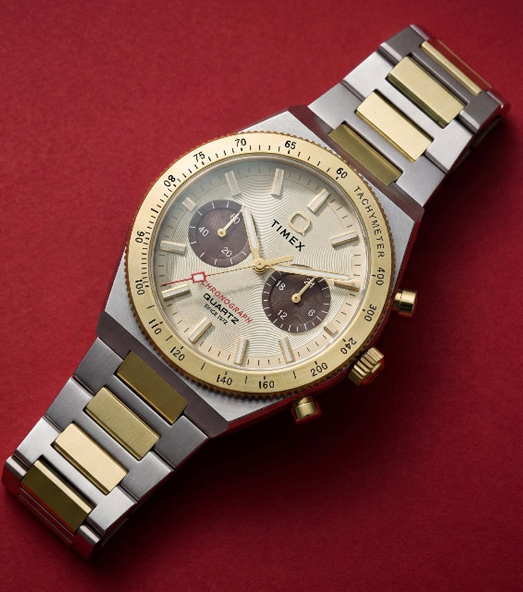 Q Timex Continental Chronograph two-tone watch with a gold-tone bezel and champagne dial on a deep red background.
