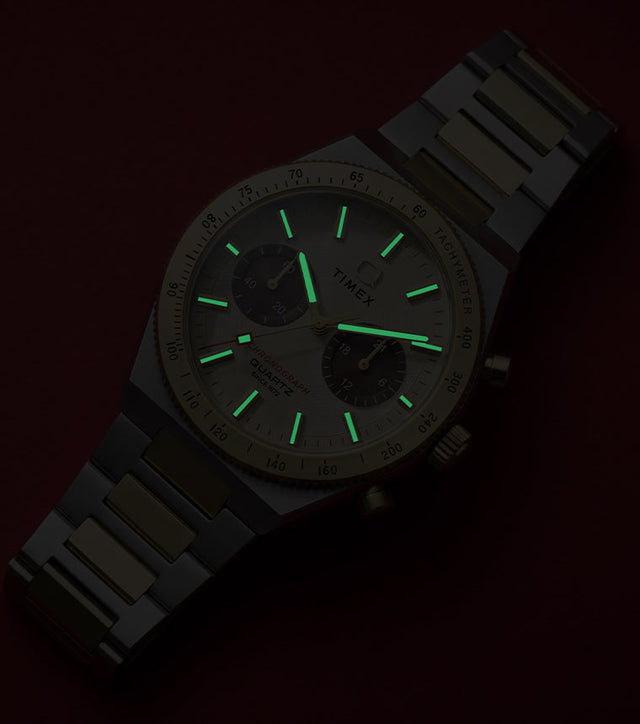 Q Timex Continental Chronograph on a dark red background with green luminous hands and hour markers visible in low light.