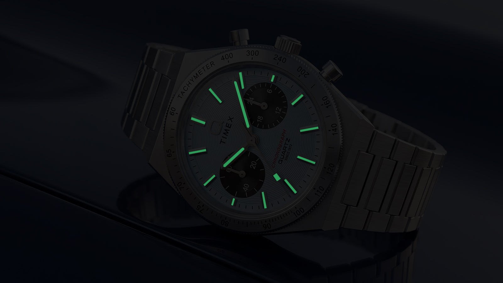 Close-up of the Q Timex Continental Chronograph in low light with green luminous hands and hour markers.