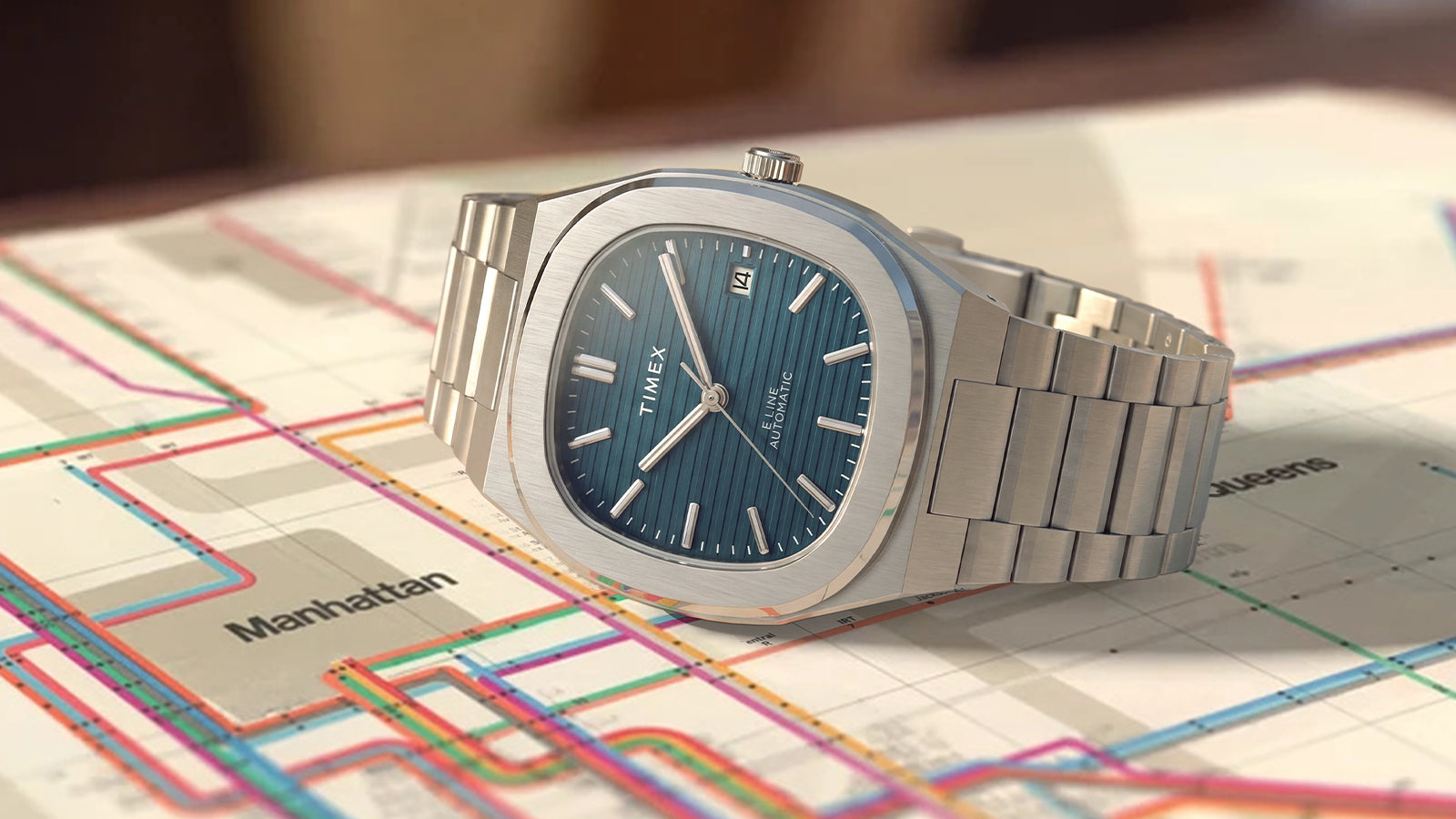Timex® Automatic E Line 38mm stainless steel watch with a blue textured dial displayed on a colorful transit map.