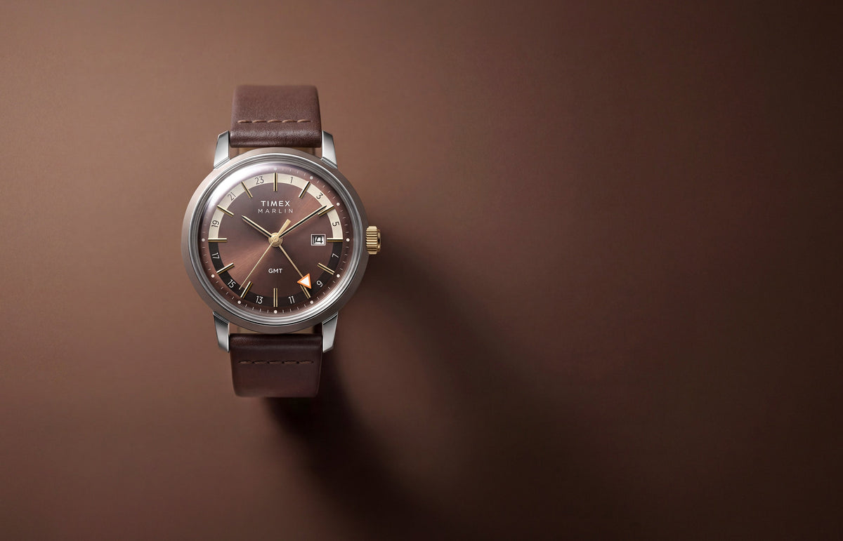 Marlin® Quartz GMT with a brown dial and leather strap displayed against a warm brown background.