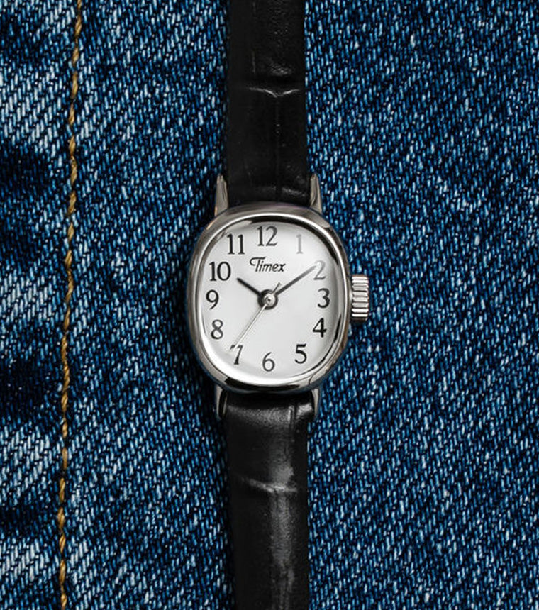 Cavatina® Mini watch with a silver-tone case, white dial, and black leather strap displayed on blue denim.