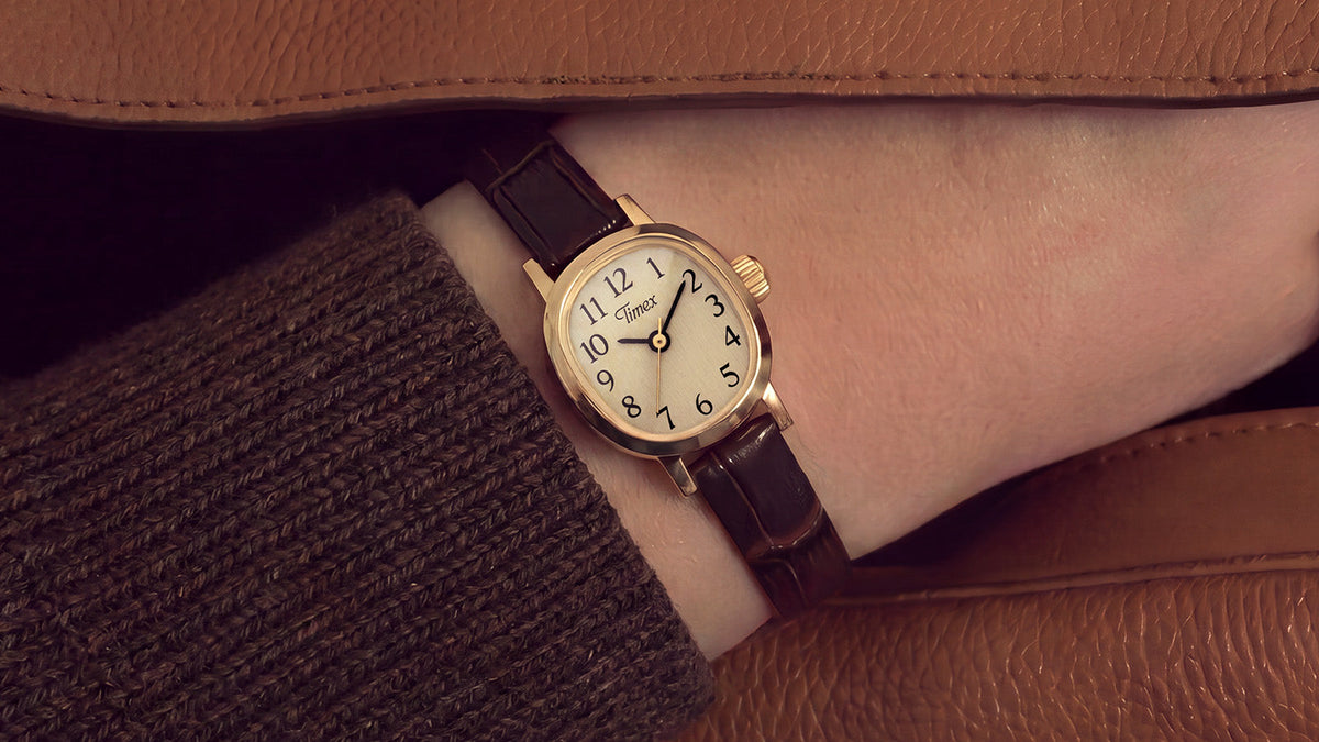 Cavatina® Mini watch with a dark brown leather strap worn on a wrist beneath a brown coat sleeve.