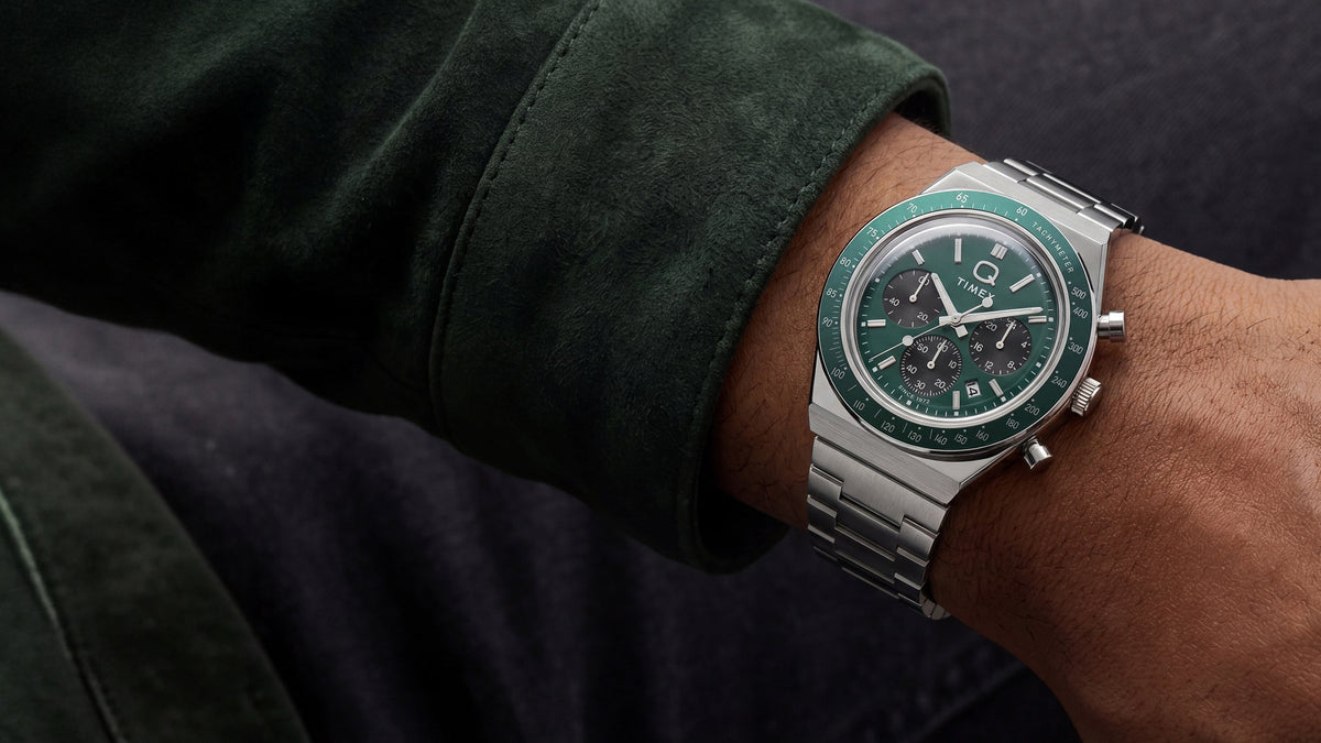 Q Timex Chronograph with a green dial and stainless-steel bracelet styled with a dark green jacket.