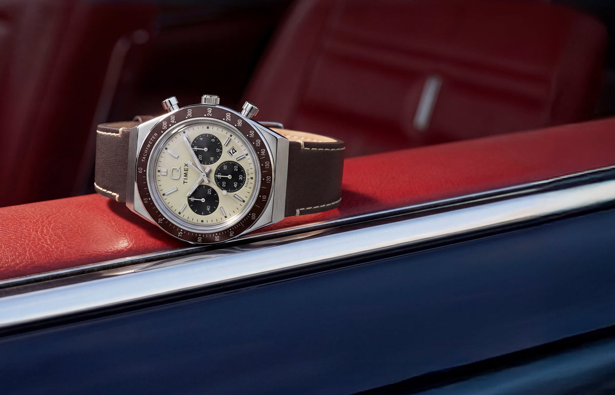Q Timex Chronograph with a cream dial and brown leather strap displayed inside a red car interior.