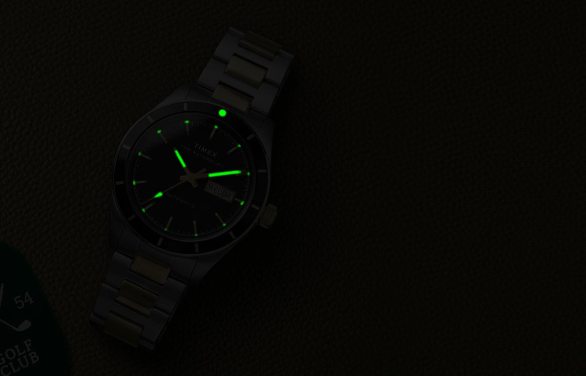 Waterbury Heritage Automatic watch illuminated by green glowing hands and hour markers on textured leather in low light.