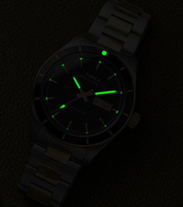 Waterbury Heritage Automatic watch illuminated by green glowing hands and hour markers on textured leather in low light.
