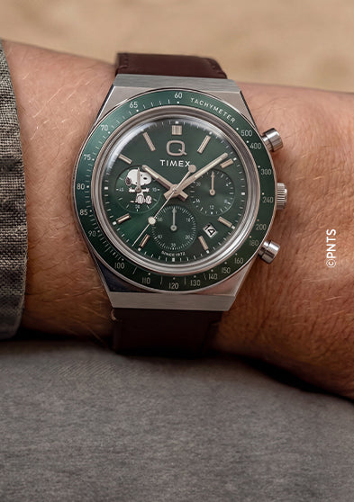 Peanuts® x Q Timex Chronograph with a green dial and brown leather strap worn on the wrist.