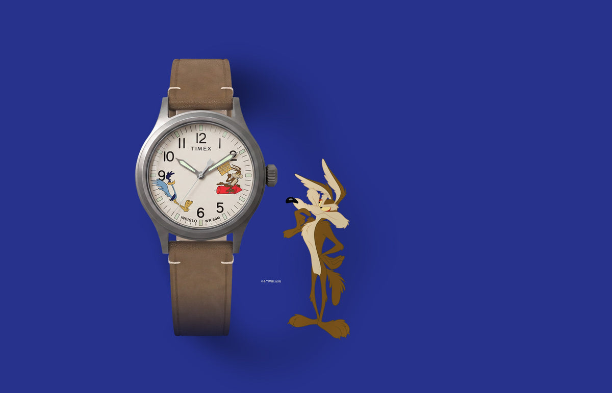 TW2Y99400 Looney Tunes Road Runner & Wile E. Coyote x Timex Expedition® Scout watch with a cream character dial and brown leather strap beside Wile E. Coyote artwork.