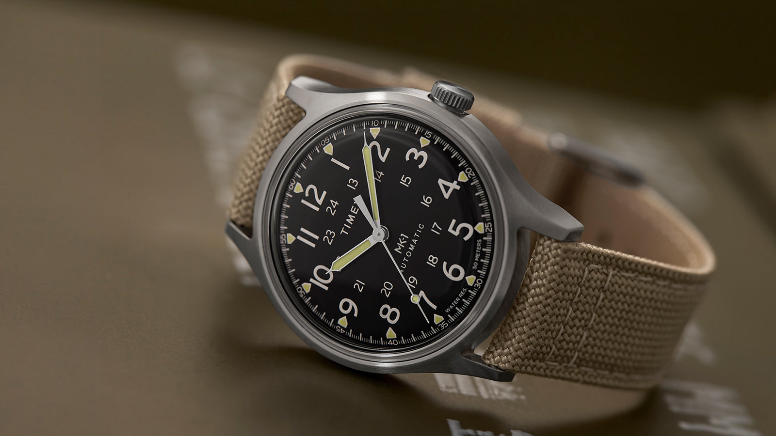 Angled close-up of the MK1® Automatic watch resting on military-style equipment.