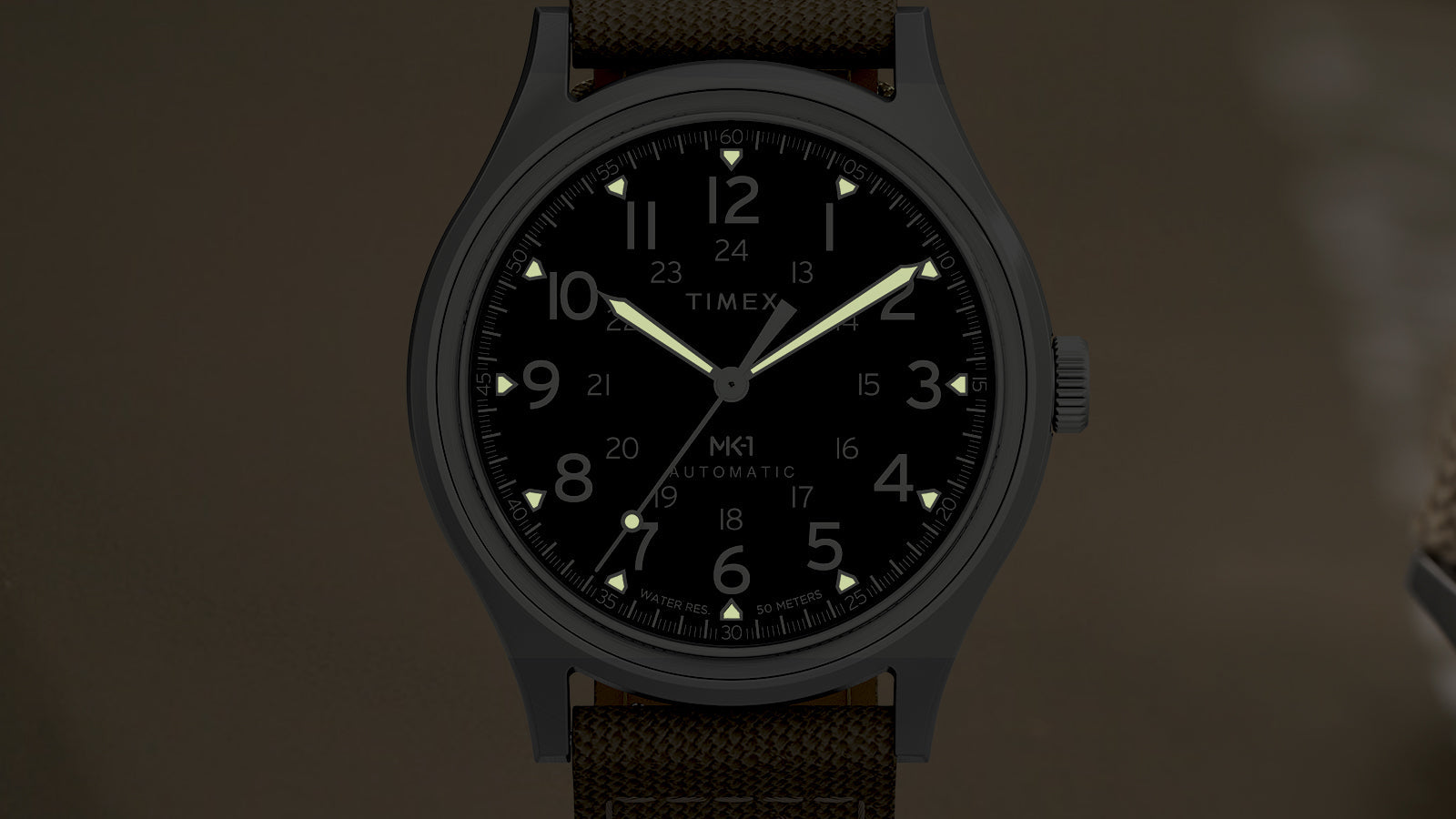 Front view of the MK1® Automatic watch in low light, showing its luminous hands and hour markers.