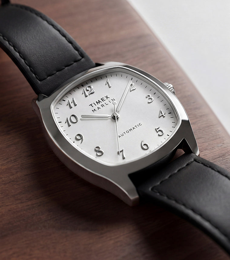 TW2Y84300 Marlin® Chatham Automatic watch with a silver-tone cushion-shaped case, white dial, and black leather strap resting on a wooden surface.