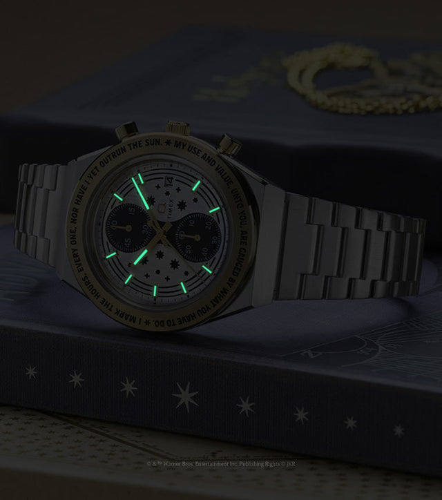 TW2Y75900 The watch and Time-Turner pendant in dim light, showing the watch’s glowing hands and hour markers.