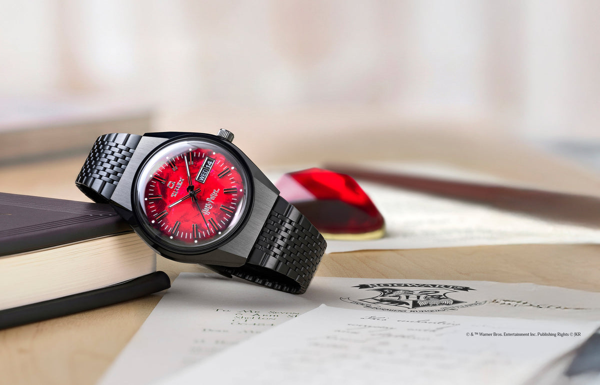 TW2Y99700 Harry Potter x Q Timex watch with a red Sorcerer’s Stone-inspired dial and black bracelet displayed beside books and a Hogwarts letter.