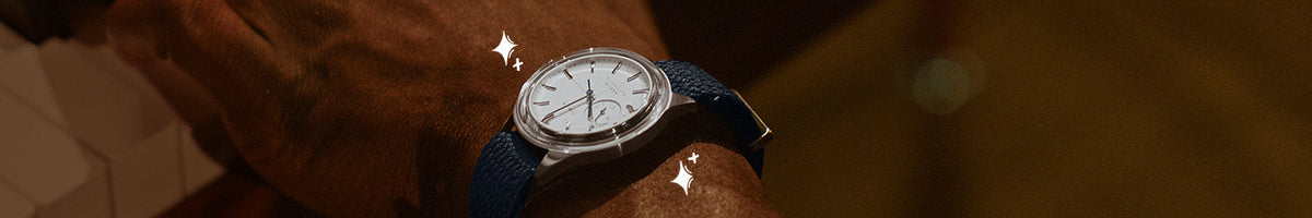 Luxe Gifts - Close-up of a Timex watch with a white dial, silver-tone case and navy strap worn on a wrist.