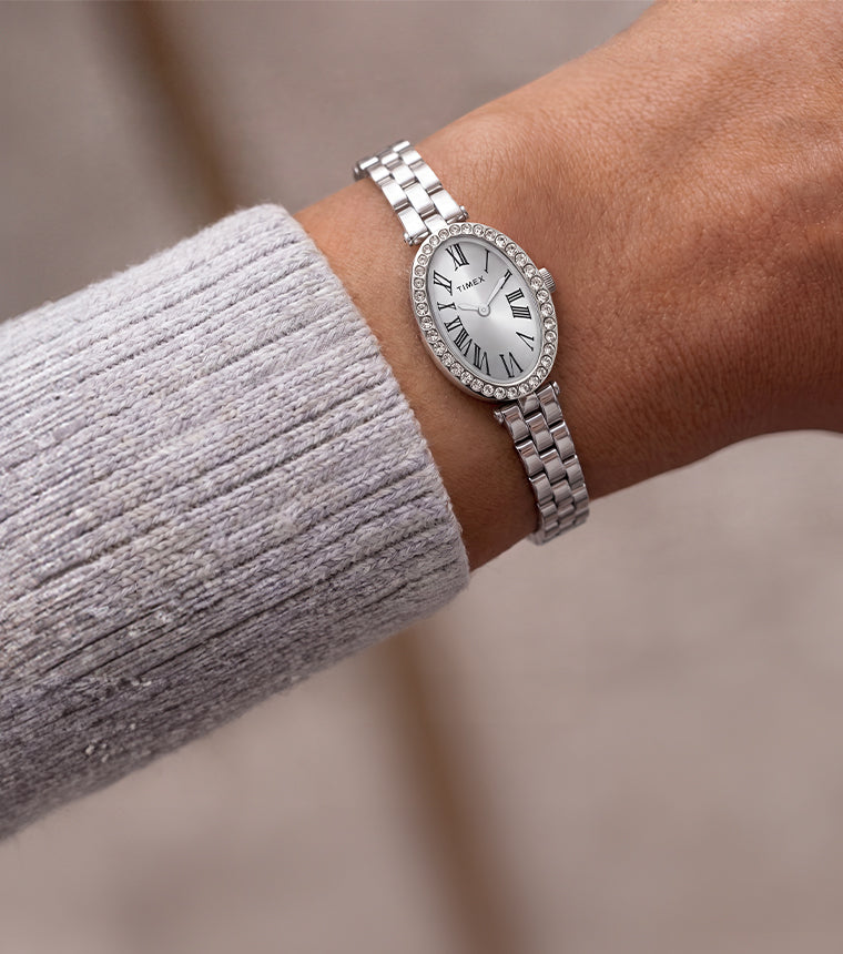 TW2Y90000 Timex Cavatina® Crystals watch with a silver-tone link bracelet and oval Roman numeral dial, worn beside a light gray knit sleeve.