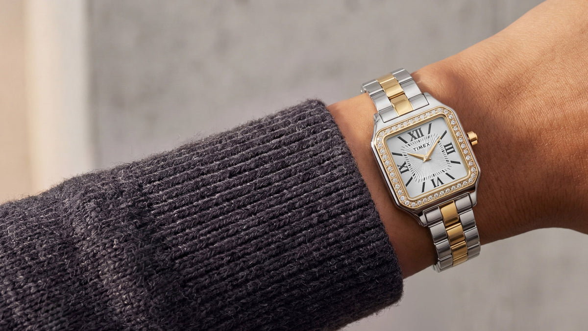 TW2Y90400 Timex Addison watch with a silver-and-gold-tone bracelet, white Roman numeral dial, and crystal-lined bezel, worn with a charcoal knit sweater.