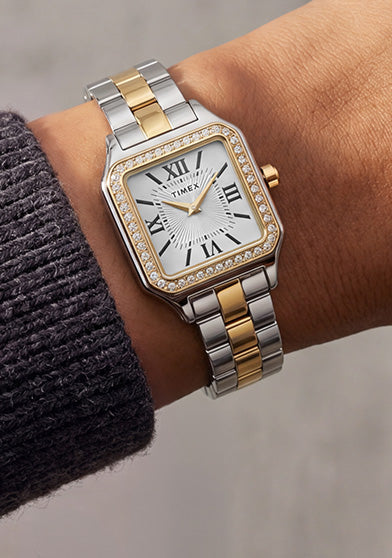 TW2Y90400 Timex Addison watch with a silver-and-gold-tone bracelet, white Roman numeral dial, and crystal-lined bezel, worn with a charcoal knit sweater.
