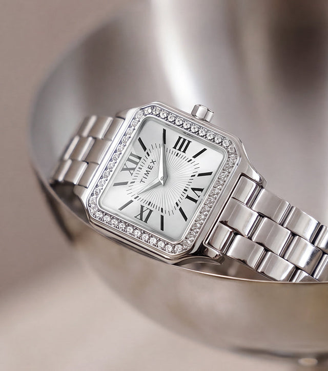 TW2Y90300 Timex Addison watch with a silver-tone bracelet, white Roman numeral dial, and crystal-lined bezel, resting in a metal dish.