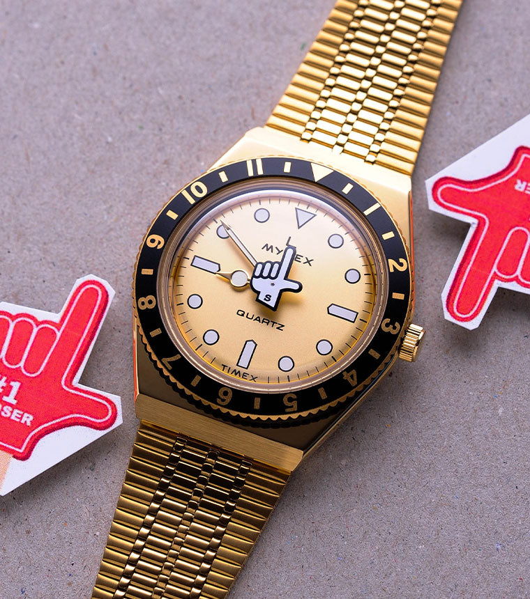 Gold seconde/seconde watch on a grey background with red hand icons either side