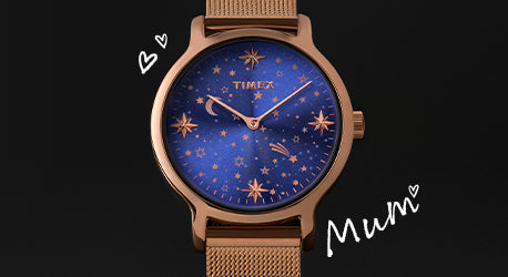 Rose gold watch with blue dial featuring star pattern. Watches is on a black background with the word Mum and some hearts. 