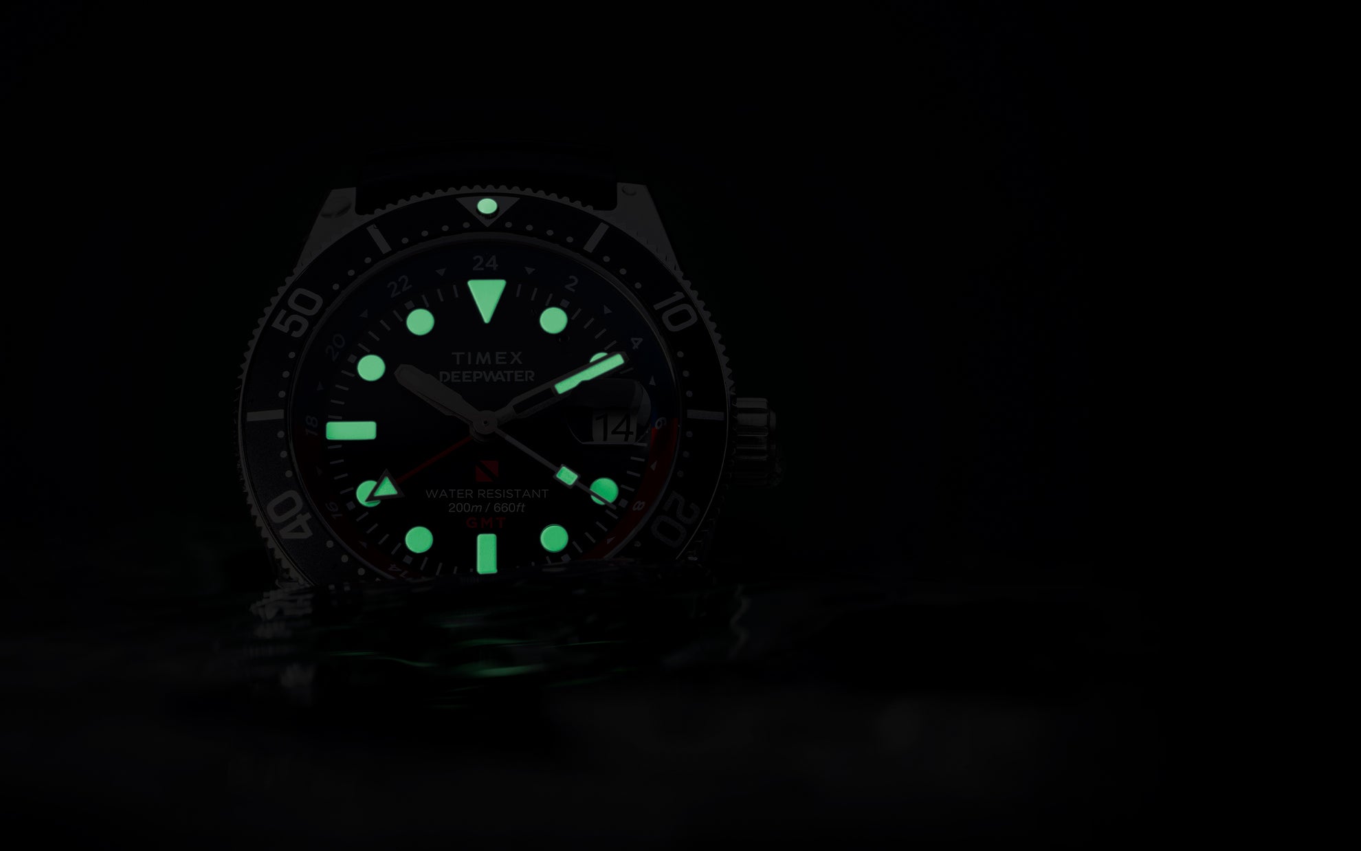 The Timex Deepwater Reef 200 GMT glowing in the dark with bright green luminous markers and hands, emphasizing legibility in low-light underwater conditions.