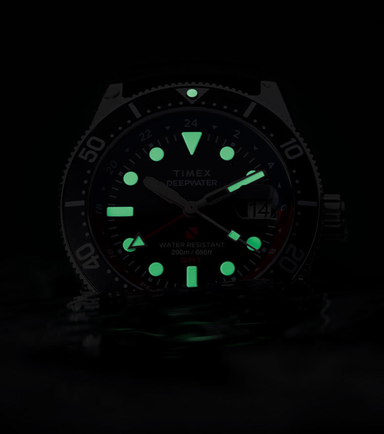 The Timex Deepwater Reef 200 GMT glowing in the dark with bright green luminous markers and hands, emphasizing legibility in low-light underwater conditions.
