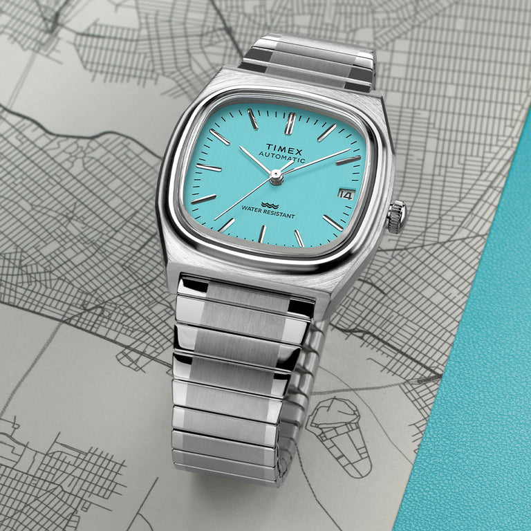 Timex® Automatic 1983 E Line watch with a turquoise dial and stainless-steel bracelet resting on a city map.