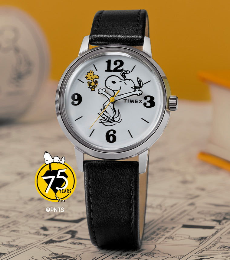 A close-up of the Timex x Peanuts® Marlin® watch featuring Snoopy and Woodstock in a playful animated design. The watch is displayed on a vintage Peanuts® comic strip background with a yellow book in the backdrop, celebrating the 75th anniversary.
