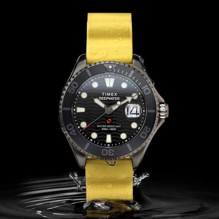 A Timex Deepwater dive watch with a black wave-pattern dial and bold luminescent hour markers, displayed vertically above a rippling water surface. The watch features a unidirectional bezel, magnified date window, and 200-meter water resistance marking. It is paired with a vibrant yellow silicone strap covered in water droplets, emphasizing its durability and aquatic performance.