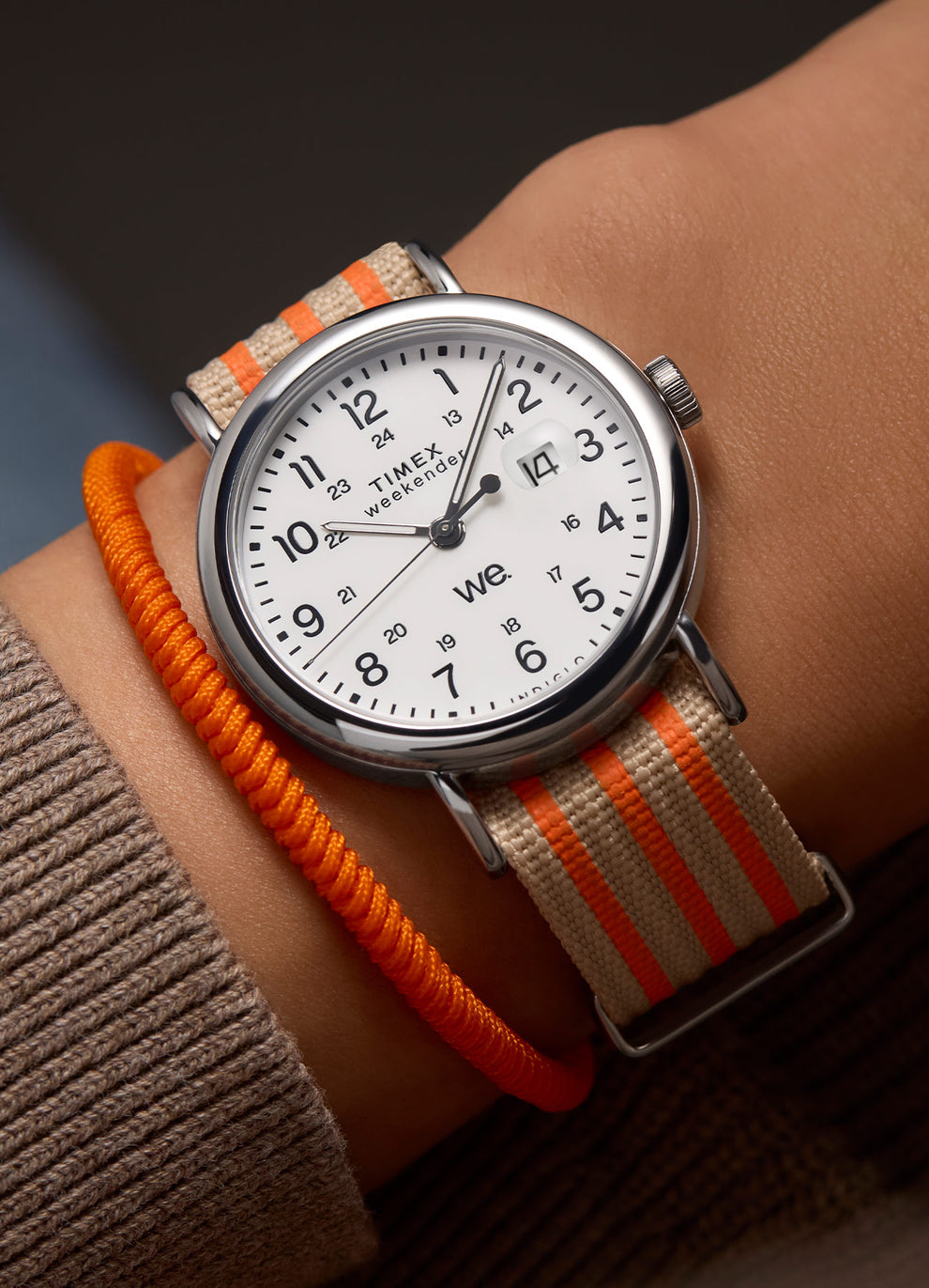 Wrist shot of the Timex Weekender with beige and orange strap, paired with an orange rope bracelet.