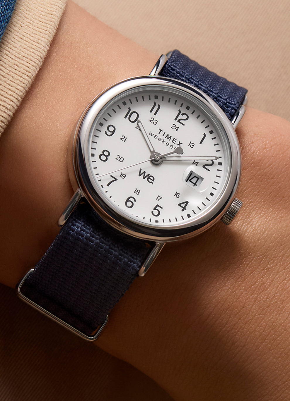 Close-up wrist shot of the Timex Weekender 37mm watch with a white dial and navy-blue strap, worn on the left wrist, paired with neutral-toned apparel.