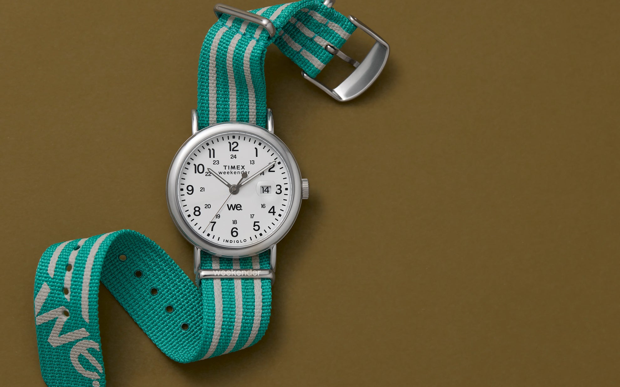 A Timex Weekender watch laid flat against a khaki background, featuring a white dial and an aqua-and-gray striped fabric strap displaying the text "weekender".