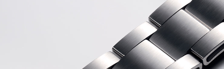 A highly detailed close-up of a titanium watch bracelet, showcasing its brushed metallic finish and interlocking design. The smooth and reflective surface highlights the craftsmanship and lightweight yet strong properties of titanium.