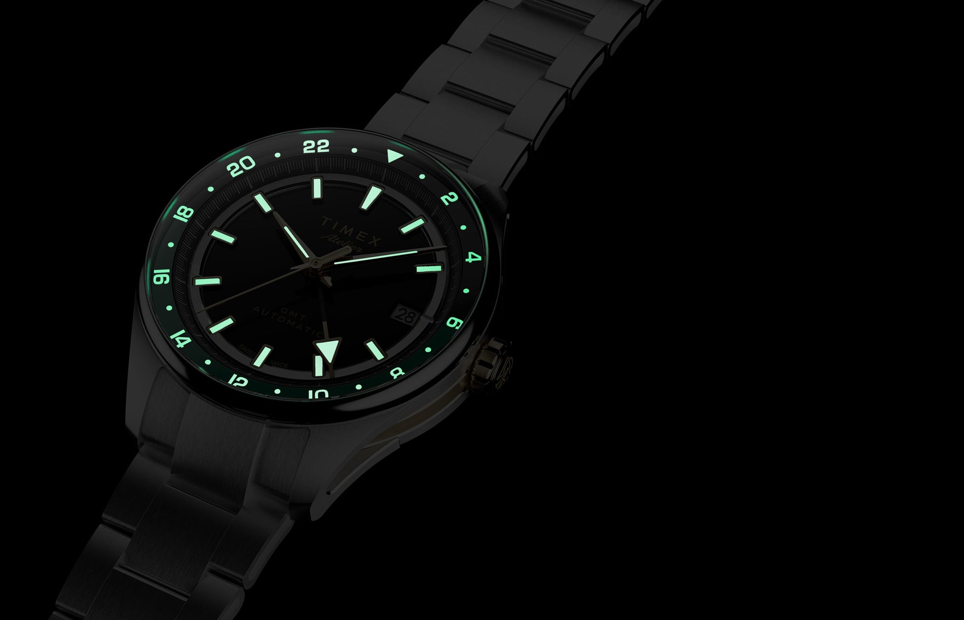 Timex Atelier GMT Première M1a watch glowing in the dark with illuminated hour markers, hands, and 24-hour scale.