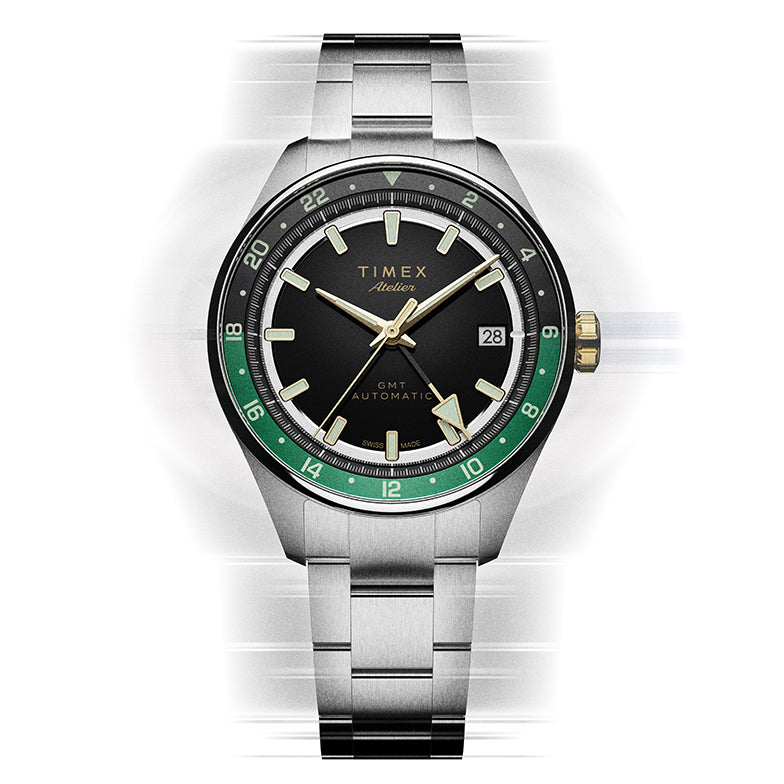 Front view of the Timex Atelier GMT Première M1a watch with a black dial, green GMT scale, and stainless-steel bracelet.