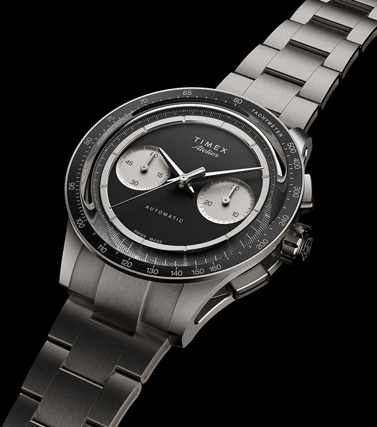 Timex Atelier Chronograph Automatic M1a Ti titanium watch with black dial, twin silver sub-dials, tachymeter bezel, and integrated titanium bracelet shown at an angled perspective.