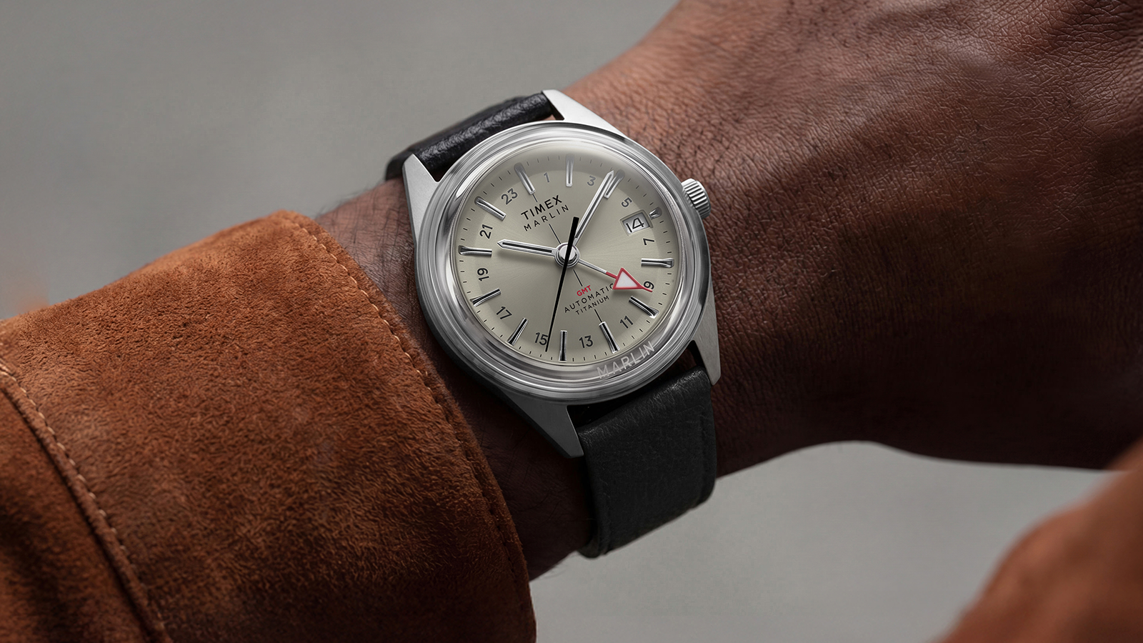 Marlin® Jet Titanium Automatic GMT watch with cream dial and black leather strap worn on the wrist with a brown suede jacket.